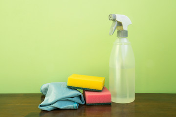 Plastic clear sprinkler, sprayer, with microfiber cloth and sponges, on a brown table and a clear background. Space to write.