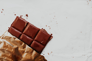 large chocolate bar broken into squares on dirty white paper with chocolate chips and gold foil around the edges.