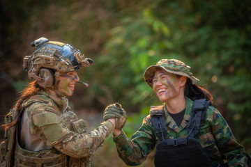 Two female soldiers are holding their hands and relax after fighting. War, soldier army, gun and...