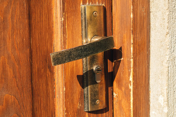 Close up of metal door handle on old wooden door in morning light.