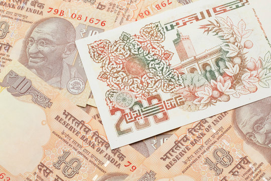 A macro image of a beige two hundred Algerian dinar bank note on a background of Indian ten rupee bank notes