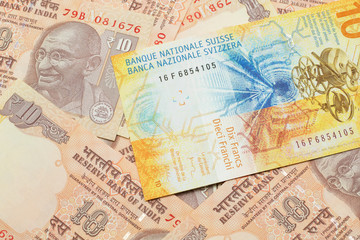 A yellow, ten Swiss franc note from Switzerland close up in macro with Indian ten rupee bank notes