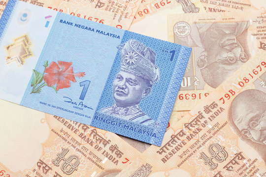 A close up image of a blue one Malaysian ringgit bank note on a bed of Indian ten rupee bank notes close up in macro