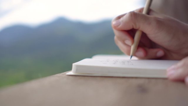 4K video of woman hand writing down in white notebook with work space beautiful nature view background.