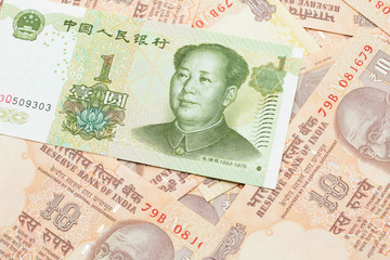 A close up image of a green, one Chinese yuan bank note, close up on a background of orange Indian ten rupee bank notes.  Shot in macro