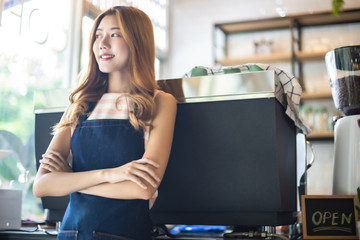 Pretty young asian waitress standing arms crossed in cafeteria.Coffee Business owner Concept.  barista in apron smiling at camera in coffee shop counter