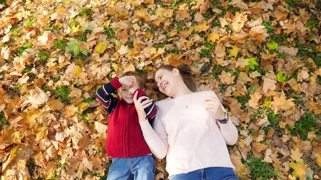 4k video of happy smiling and laughing little boy with young mother lying on grass and leaves at autumn park