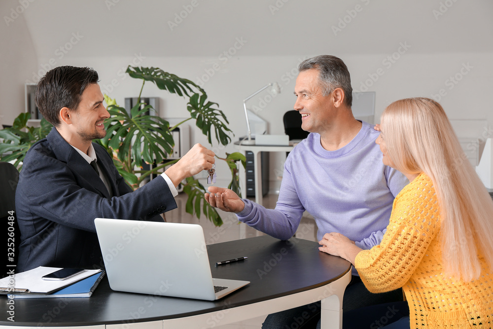 Poster real estate agent giving a key from new house to mature couple in office