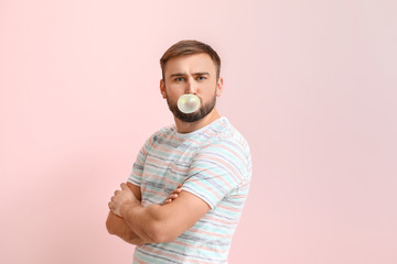 Funny man with chewing gum on color background