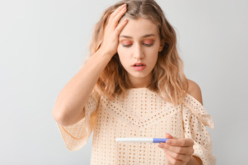 Sad young woman with pregnancy test on light background