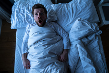 Man had a nightmare, he woke up and screamed in horror, scaredly looking into the camera with big eyes. Concept of insomnia.