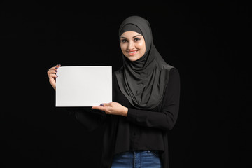 Young Arab woman with blank paper sheet on dark background