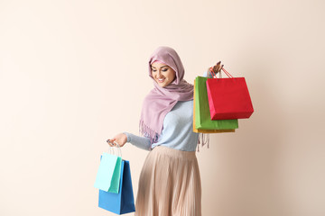 Young Arab woman with shopping bags on color background