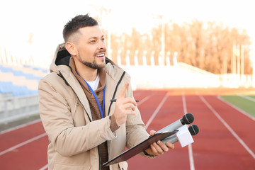Male reporter with microphones at the stadium