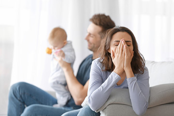 Happy father with his baby and wife suffering from postnatal depression at home