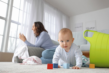 Mischievous baby with careless young mother at home
