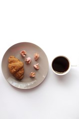 Breakfast with croissant on the plate with coffee and decorated flowers top view