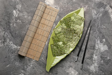 Plate with tasty seaweed sheets, bamboo mat and chopsticks on table