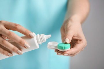 Woman pouring solution in container with contact lenses, closeup