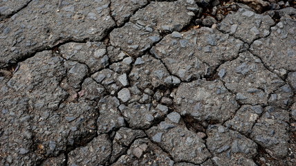 Damaged asphalt road, cracked cracks and scattered stones, with selective focus