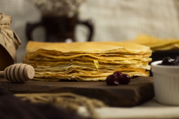 Stack of fresh pancakes for Shrovetide with jam, honey and willow branches. On a wooden Board in the Russian style. Pancake week