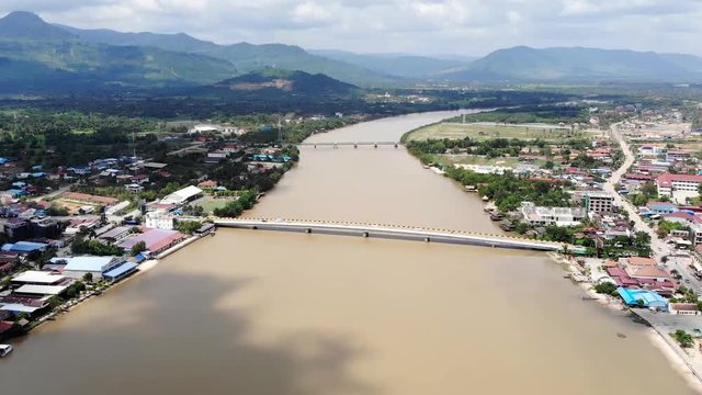 Flying over the Praek Tuek Chhu River in Kampot, Cambodia. Neighborhoods on either side of the river, with mountains and clouds in the background.