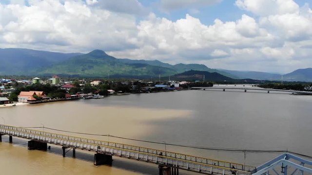 Flying up and panning to the right over the Praek Tuek Chhu River in Kampot, Cambodia. Homes and beautiful big mountains in the background.