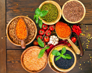 Wooden bowls of various lentils with red and green hot chilli peppers with leaves and tomatoes on a wooden background. Top view.