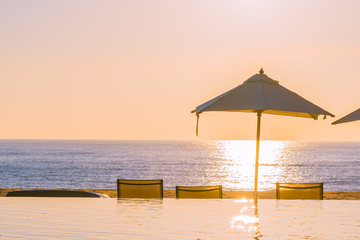 Beautiful tropical outdoor beach sea ocean with umbrella and chiar around outdoor swimming pool at sunset or sunrise time