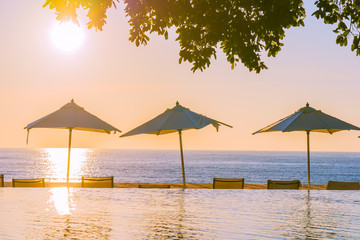 Beautiful tropical outdoor beach sea ocean with umbrella and chiar around outdoor swimming pool at sunset or sunrise time