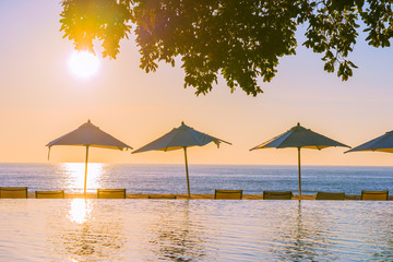 Beautiful tropical outdoor beach sea ocean with umbrella and chiar around outdoor swimming pool at sunset or sunrise time