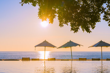 Beautiful tropical outdoor beach sea ocean with umbrella and chiar around outdoor swimming pool at sunset or sunrise time