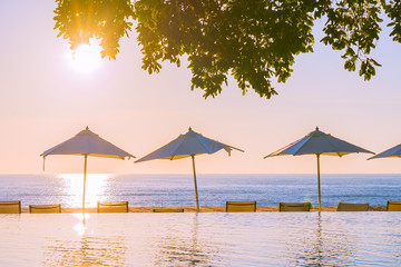 Beautiful tropical outdoor beach sea ocean with umbrella and chiar around outdoor swimming pool at sunset or sunrise time