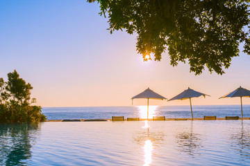 Beautiful tropical outdoor beach sea ocean with umbrella and chiar around outdoor swimming pool at sunset or sunrise time