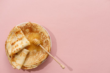 Delicious homemade pancakes with honey on a gently pink background. Top view, close-up. Traditional holiday celebration concept. Russian translation wide and happy Shrovetide Maslenitsa.