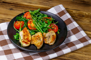 Fried chicken breast with salad of fresh arugula and cherry tomatoes on wooden table