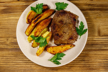 Fried beef steak with potato wedges on wooden table. Top view