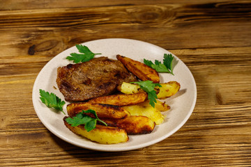 Fried beef steak with potato wedges on wooden table
