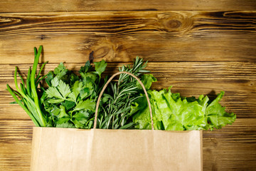 Paper bag with green onion, rosemary, lettuce leaves and parsley on wooden table. Top view. Healthy food and grocery shopping concept