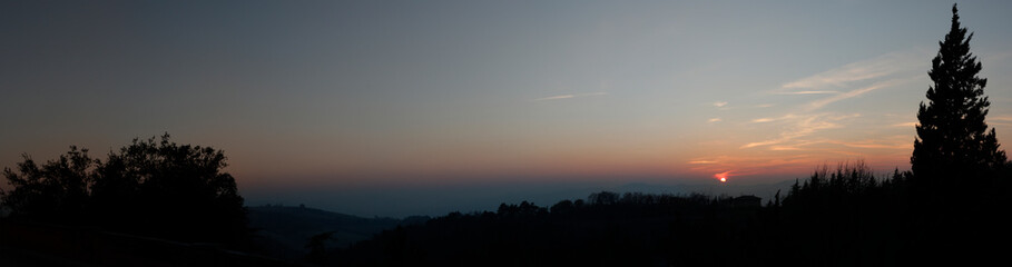 late night panoramic view of the sunset. Red sun, tree silhouettes, skyline.