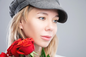 Close-up portrait of an attractive caucasian blonde girl in a retro cap with roses in her hands and looking to the side