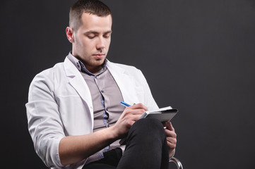 Portrait of a young intern doctor. A man sits on a chair with a notebook and pen in his hands and...