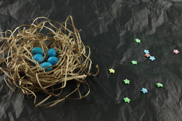 Small blue eggs of a bird lie in a nest made of straw on a black background. The Easter theme.  Selective focus