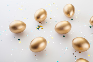 Golden eggs on a white background, sprinkled with sequins. The Concept Of Easter.