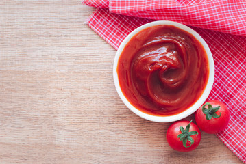 Tomato ketchup sauce in ceramic bowl on placemat with tomatoes over wooden background.
