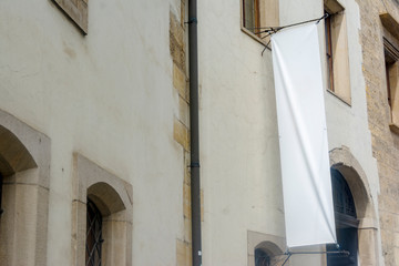 Light wall of an old building with a white blank vertical banner for an inscription or advertising image