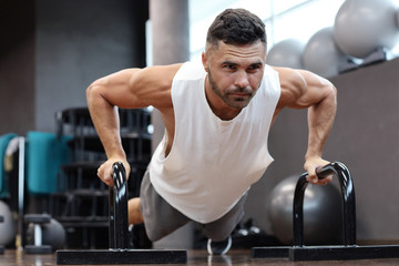Fit and muscular man doing horizontal push-ups with bars in gym.