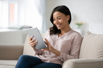 Smiling african American woman busy browsing tablet - Powered by Adobe