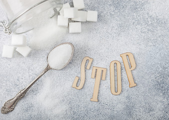 Glass jar of natural white refined sugar with cubes with silver spoon on light table background with STOp letters. Unhealthy food concept. Top view