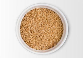 Glass bowl of natural brown refined sugar on white background.